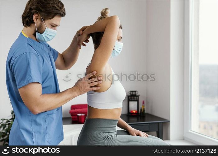side male osteopathic therapist with medical mask checking female patient s shoulder joint