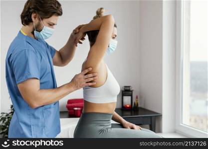 side male osteopathic therapist with medical mask checking female patient s shoulder joint