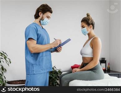 side male osteopathic therapist with medical mask female patient office signing clipboard