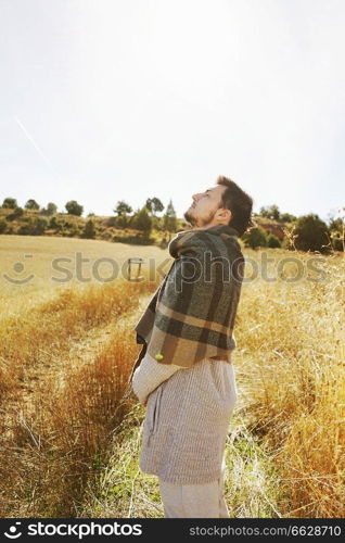 Side of a stand young man enjoying in calm the morning autumn sun in a path of a yellow field with the backlight from the blue sky