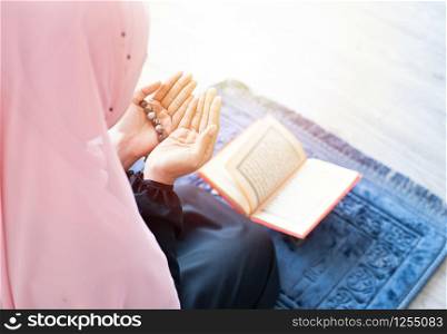 side of asian young beautiful muslim woman pray with beads and read quran sit on carpet mat with meditation in mosque.