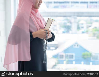 side of asian young beautiful muslim woman pray with beads and read quran sit on carpet mat with meditation in mosque.