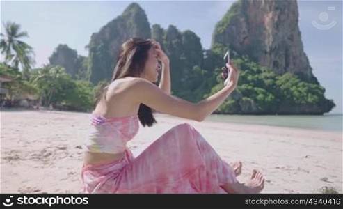 Side portrait a young beautiful asian woman making video call on smartphone, cheerfully talking with waving her hand to a new friend, female solo travel on tropical island beach trip, wireless network
