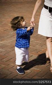 Side profile of a baby boy holding his mother&acute;s hand and walking