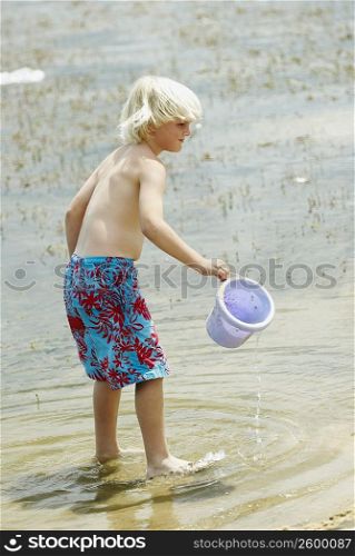 Side profile of a boy holding a sand pail and standing in water
