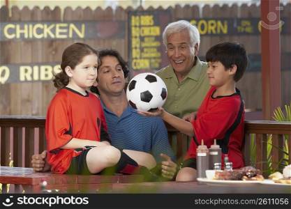 Side profile of a boy holding a soccer ball with his family beside him in a restaurant