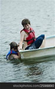 Side profile of a boy sitting in a boat with his friend swimming beside him
