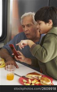 Side profile of a boy teaching his grandfather how to use a mobile phone