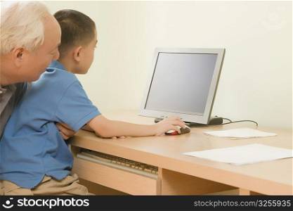 Side profile of a boy using a desktop pc with his grandfather