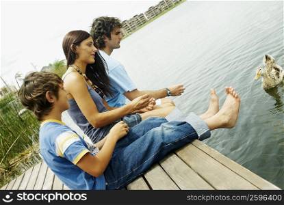Side profile of a boy with his parents feeding a duck at a lake