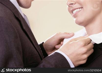 Side profile of a businessman adjusting a businesswoman&acute;s collar