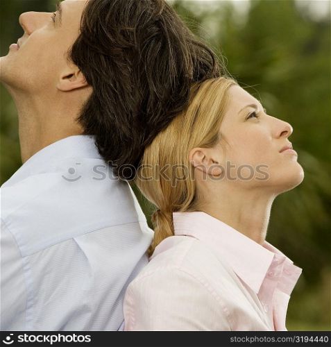 Side profile of a businessman and a businesswoman sitting back to back in the park