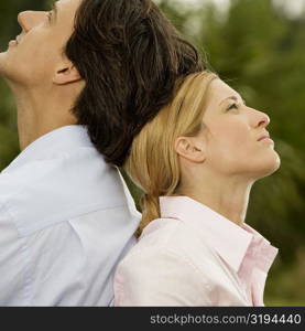 Side profile of a businessman and a businesswoman sitting back to back in the park