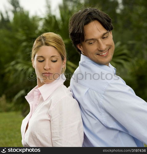 Side profile of a businessman and a businesswoman sitting back to back in the park