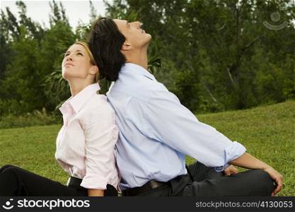 Side profile of a businessman and a businesswoman sitting back to back in the park