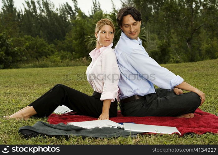 Side profile of a businessman and a businesswoman sitting back to back in the park