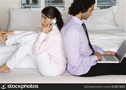 Side profile of a businessman and a businesswoman sitting back to back on the bed