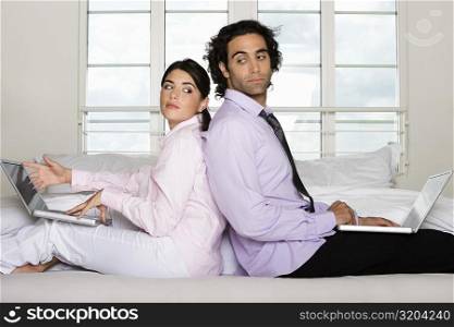Side profile of a businessman and a businesswoman sitting back to back on the bed