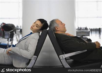 Side profile of a businessman and a businesswoman sleeping on chairs at an airport