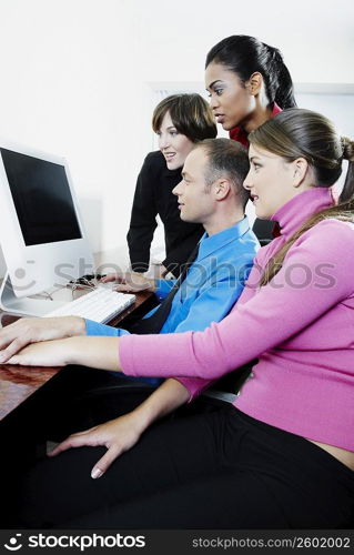 Side profile of a businessman and three businesswomen using a desktop PC