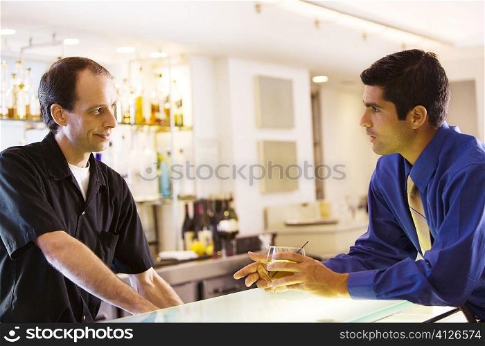 Side profile of a businessman holding a glass talking to a bar tender