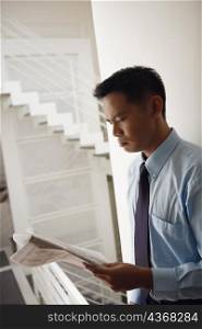Side profile of a businessman leaning against a wall and reading a newspaper