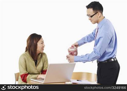Side profile of a businessman pouring tea into a teacup in front of a businesswoman