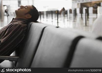 Side profile of a businessman reclining on a bench at an airport