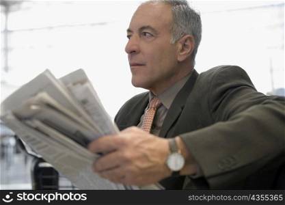 Side profile of a businessman sitting at an airport and holding a newspaper