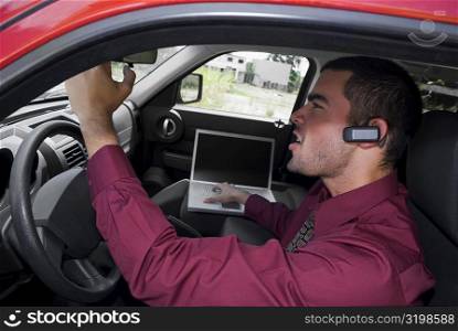Side profile of a businessman sitting in a car and using a laptop