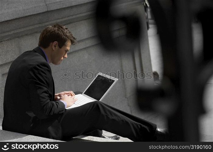 Side profile of a businessman sitting on steps and using a laptop