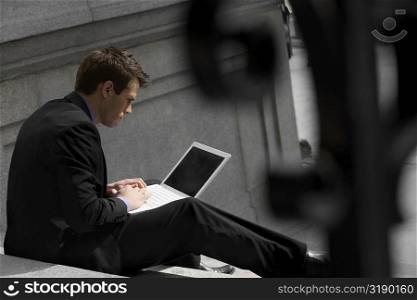 Side profile of a businessman sitting on steps and using a laptop