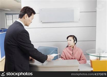 Side profile of a businessman standing in an office talking to the receptionist