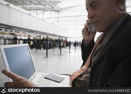Side profile of a businessman talking on a mobile phone and using a laptop at an airport lounge