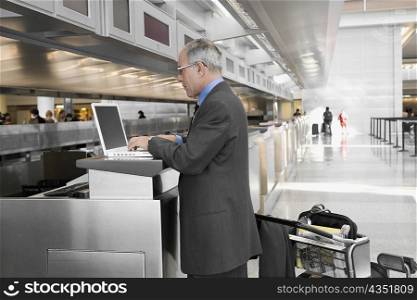 Side profile of a businessman using a laptop at an airport check-in counter