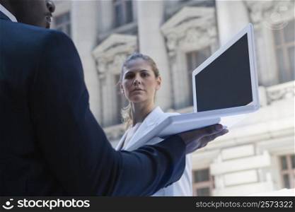 Side profile of a businessman using a laptop with a businesswoman standing in front of him