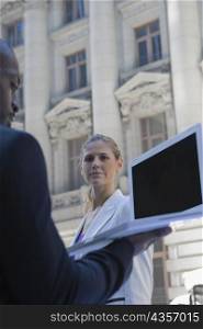 Side profile of a businessman using a laptop with a businesswoman standing in front of him