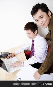 Side profile of a businessman using a laptop with another businessman smiling