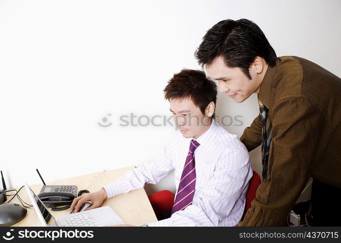 Side profile of a businessman using a laptop with another businessman standing behind him