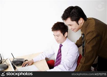 Side profile of a businessman using a laptop with another businessman standing behind him