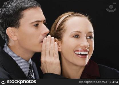 Side profile of a businessman whispering to a businesswoman