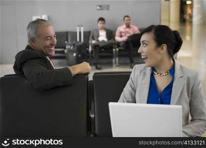 Side profile of a businessman with a businesswoman looking at each other and smiling at an airport