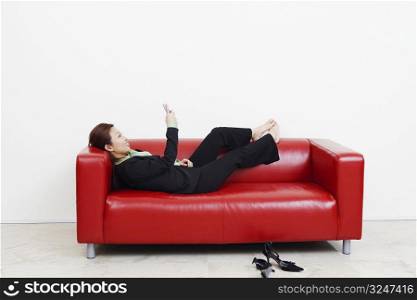 Side profile of a businesswoman lying on a couch and operating a mobile phone