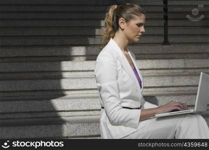 Side profile of a businesswoman sitting on a staircase and using a laptop