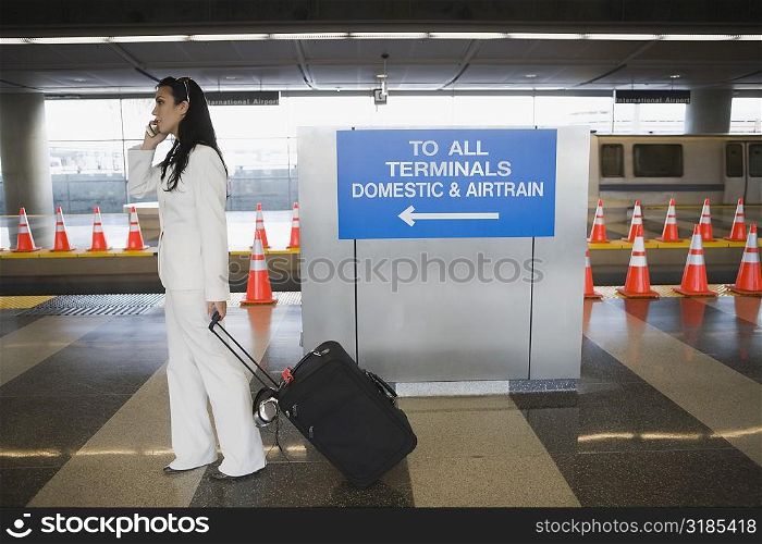 Side profile of a businesswoman talking on a mobile phone and pulling her luggage at a subway station