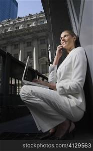 Side profile of a businesswoman talking on a mobile phone and using a laptop