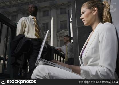 Side profile of a businesswoman using a laptop with two businessmen in the background