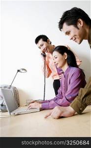 Side profile of a businesswoman using a laptop with two businessmen standing beside her