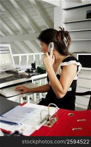 Side profile of a businesswoman using a mobile phone and working on a desktop PC