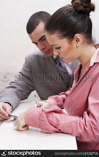 Side profile of a businesswoman writing with a businessman holding a credit card beside her